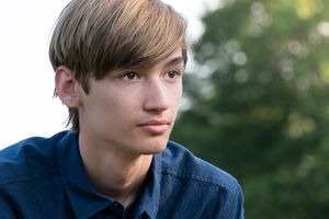 Outdoor portrait showing a young person in a navy blue shirt with natural lighting and bokeh background.
