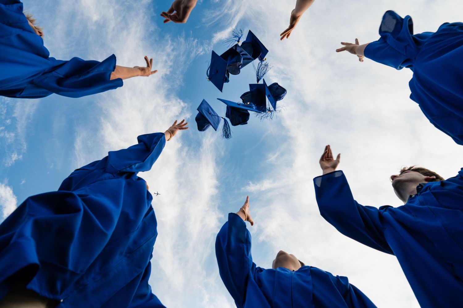 Graduating students throwing blue caps into the air against a bright sky during celebration.