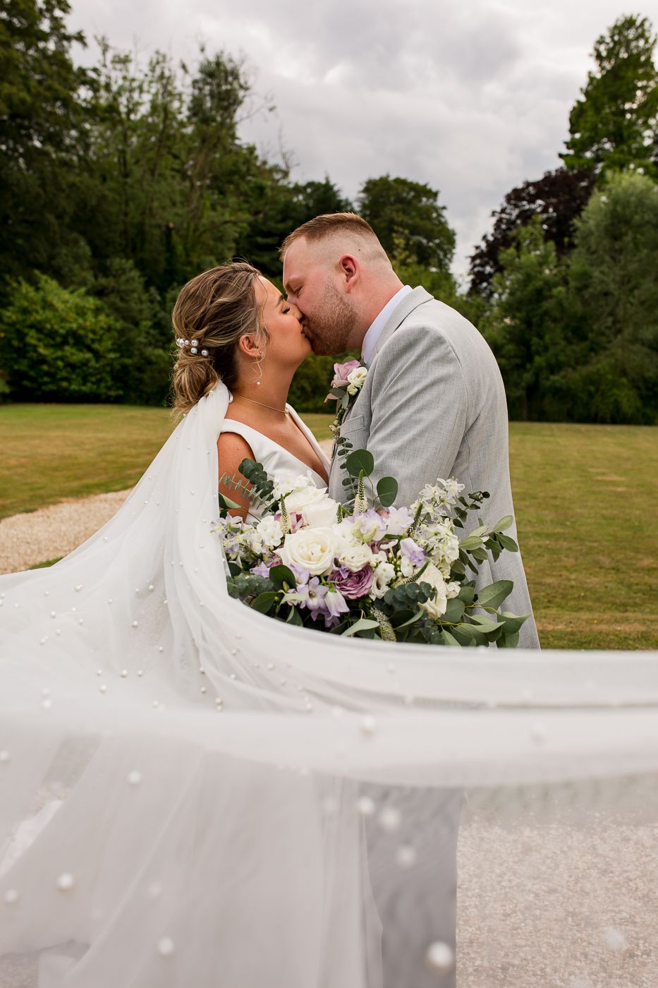 Romantic wedding portrait with flowing veil against cloudy countryside backdrop.