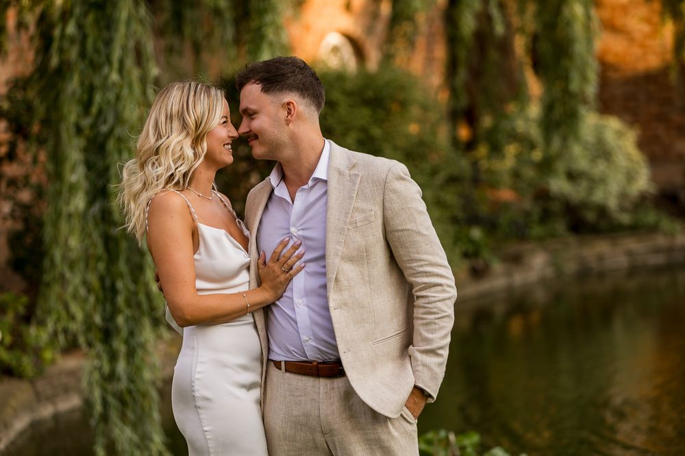 Romantic couple shares tender moment by pond with weeping willow trees.