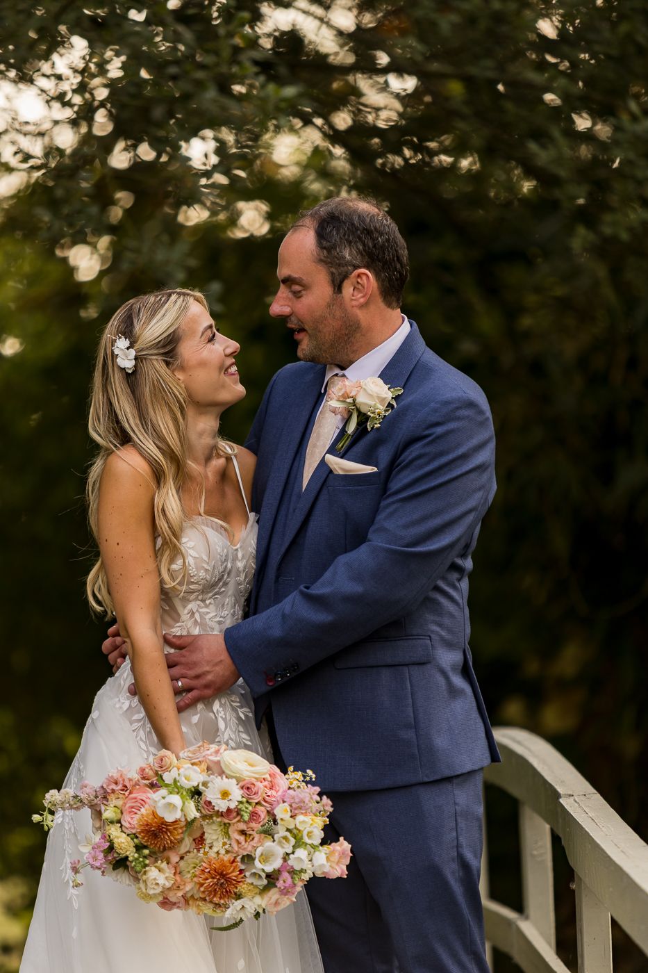 Newlyweds embrace outdoors with colorful floral bouquet at sunset.