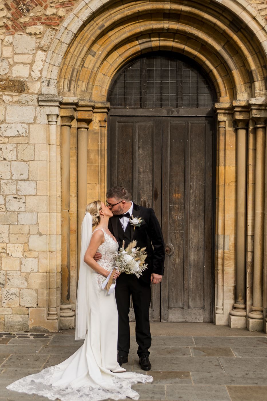 Wedding couple shares intimate moment in front of historic stone archway with ornate columns.