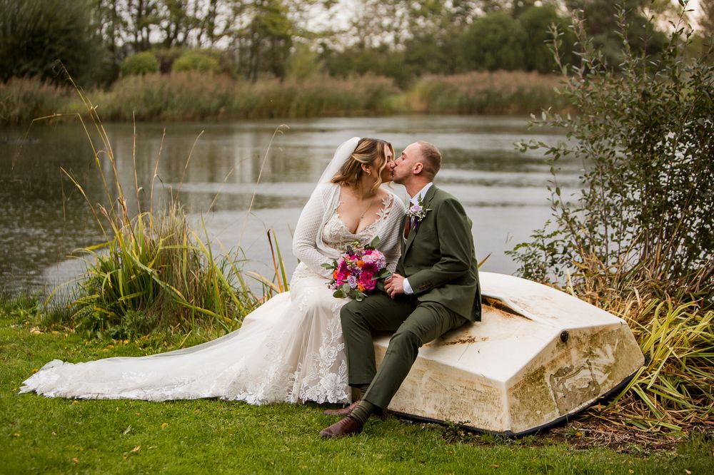 Newlyweds share romantic moment on rustic stone bench by autumn lake.