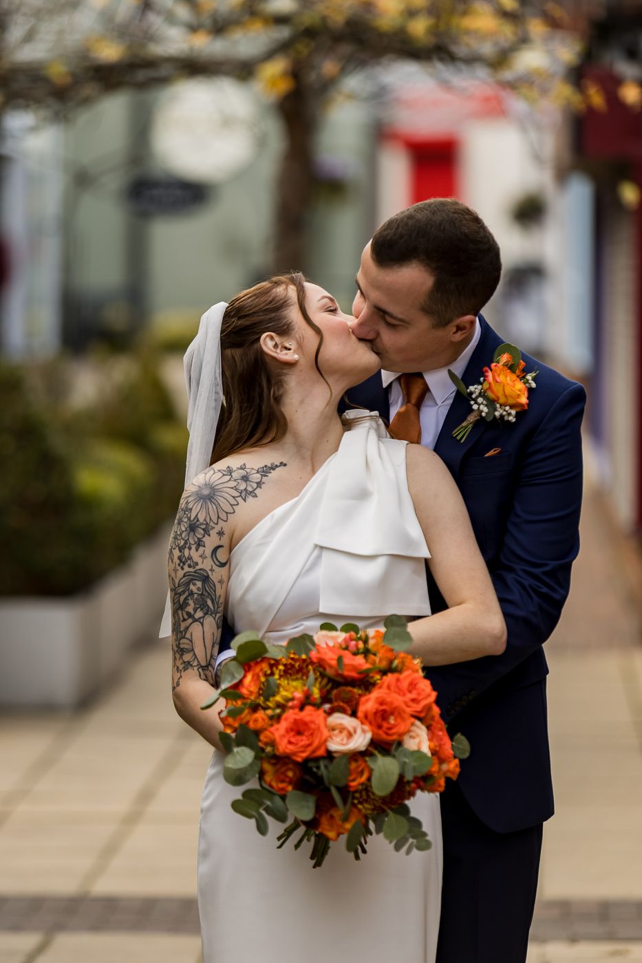 Autumn wedding bouquet features vibrant orange and peach roses against urban backdrop.