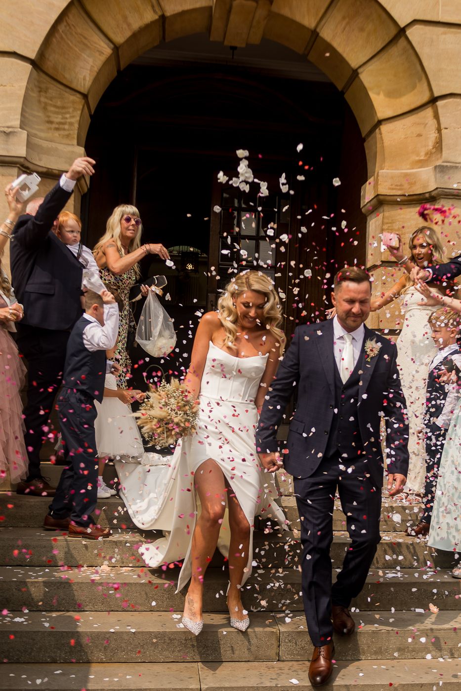 Wedding celebration with confetti being thrown under stone archways.
