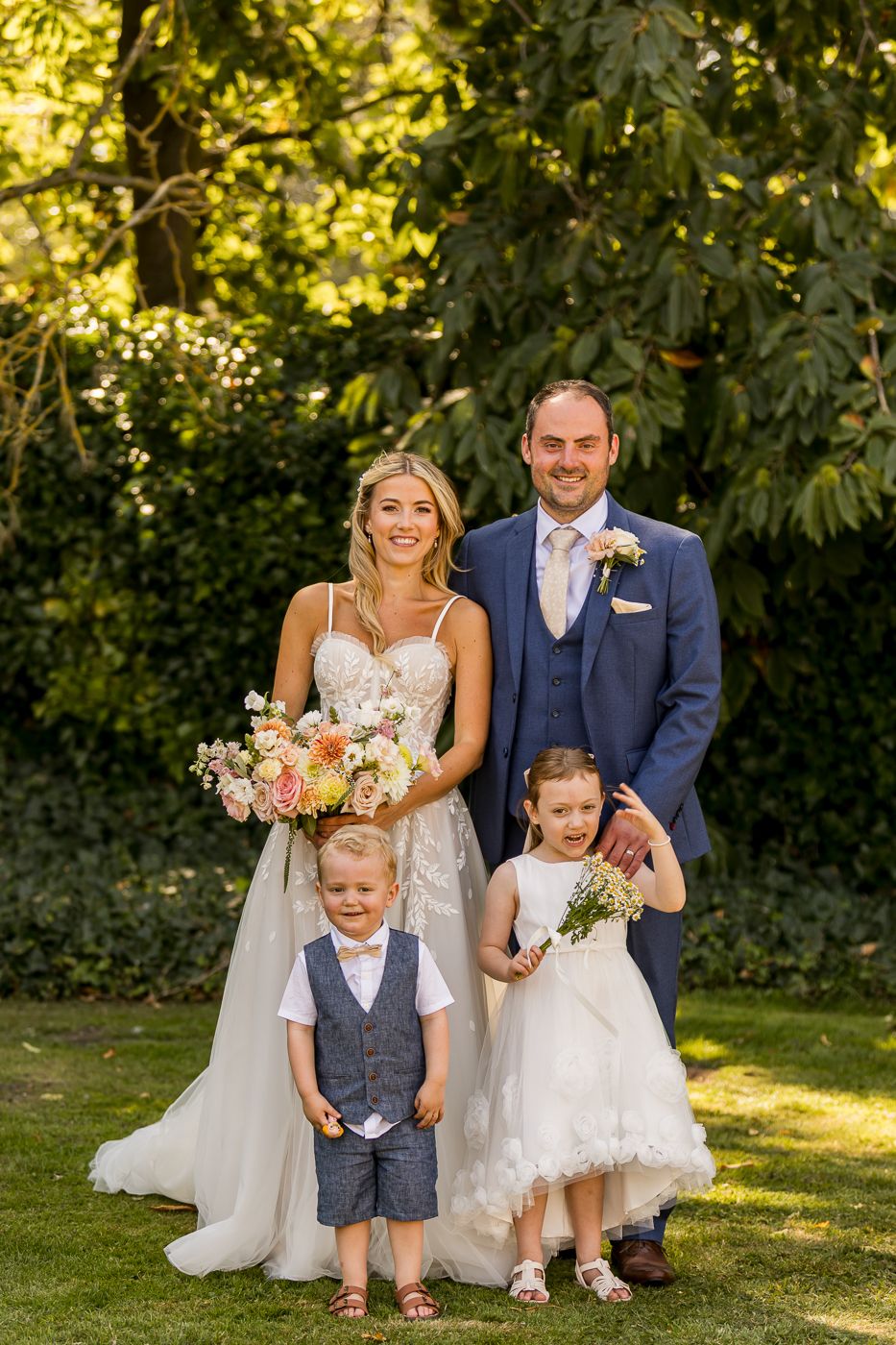 Sunny garden wedding portrait with family members on manicured lawn.