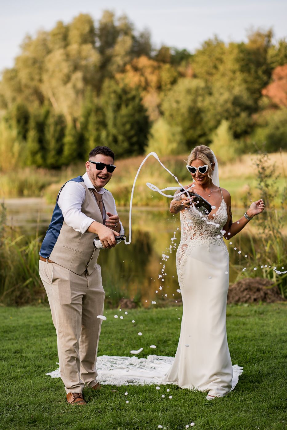 A celebratory moment on a lawn near a pond with confetti and sunglasses on a sunny wedding day.