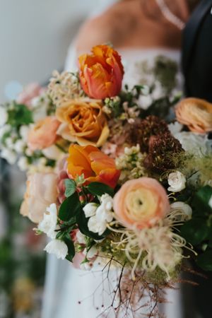 A romantic wedding bouquet with peach and orange roses, ranunculus, and delicate white flowers arranged naturally.