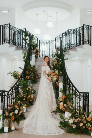Ornate staircase adorned with lush peach and orange floral arrangements and candles in an elegant white venue.