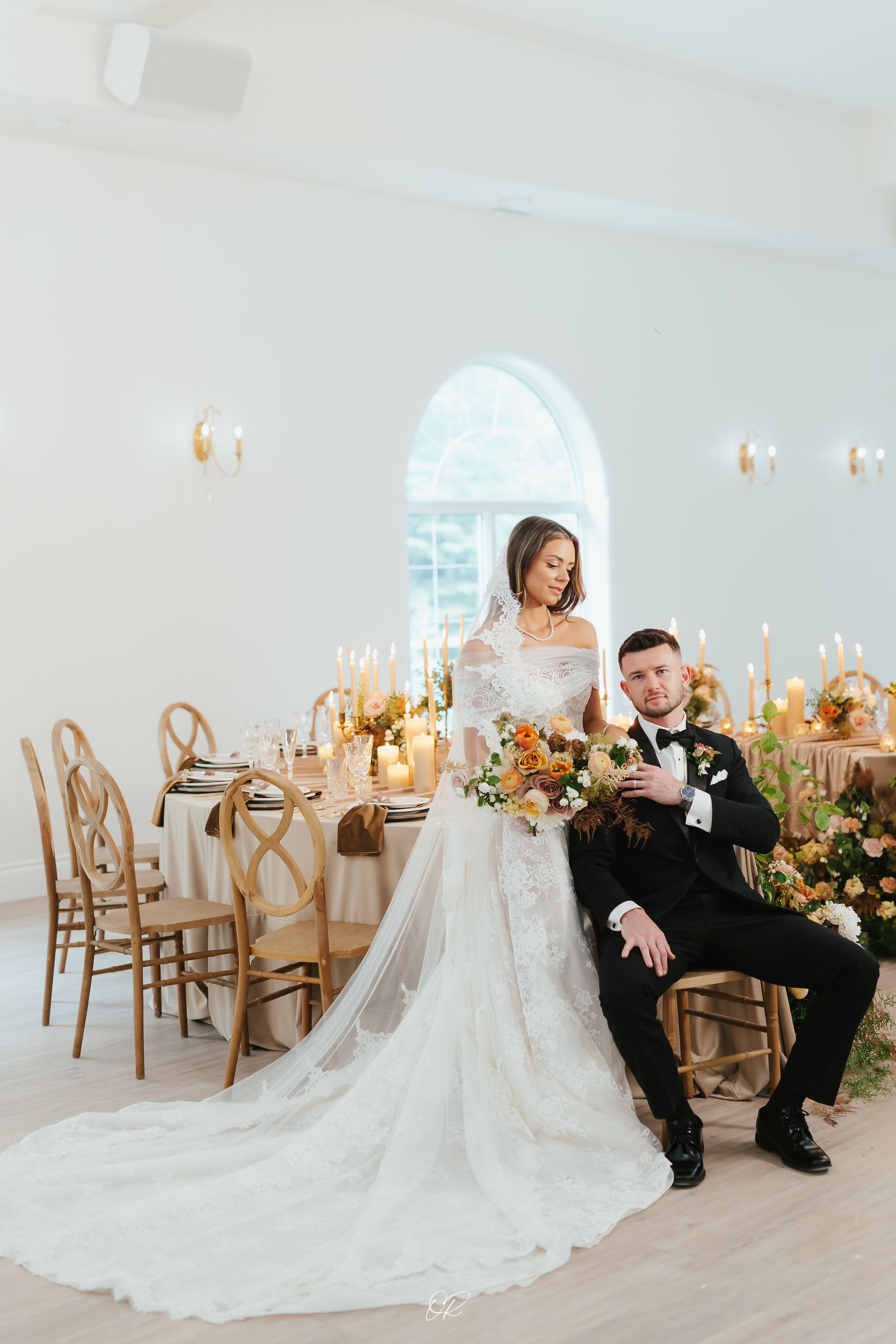 Elegant wedding reception setup with gold chairs and candlelit tables in a bright white venue.