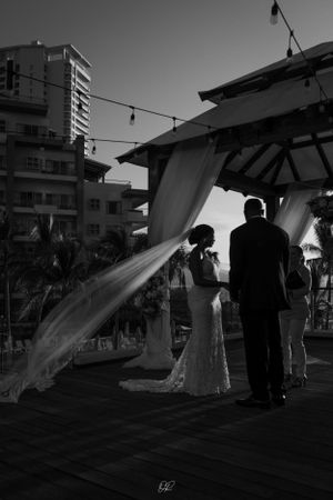 A black and white wedding scene under a gazebo with a flowing veil caught in the wind during an outdoor ceremony.