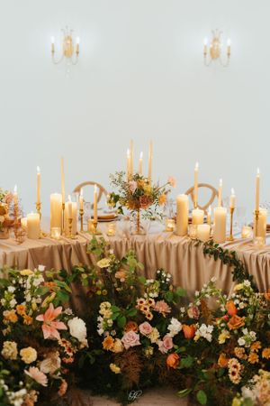 Romantic candlelit table with gold taper candles and lush floral arrangements in peach and cream blooms.