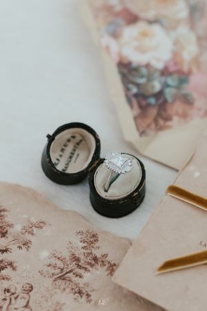 A sparkling diamond engagement ring sits in a black velvet box beside vintage floral stationery.
