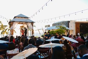 Wedding celebration at an outdoor rooftop venue with string lights and a white gazebo during sunset.