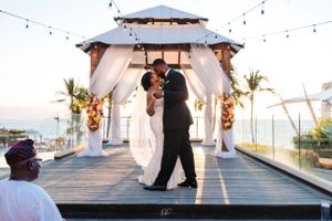 Couple sharing romantic dance moment under gazebo with string lights and ocean view.