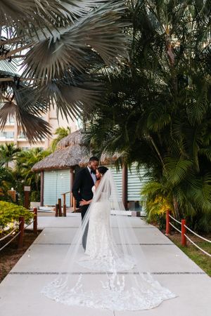 A wedding couple sharing an intimate moment on a walkway surrounded by tropical palm trees.