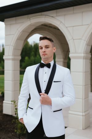 Formal white dinner jacket with black shawl collar and bow tie photographed against stone archway.