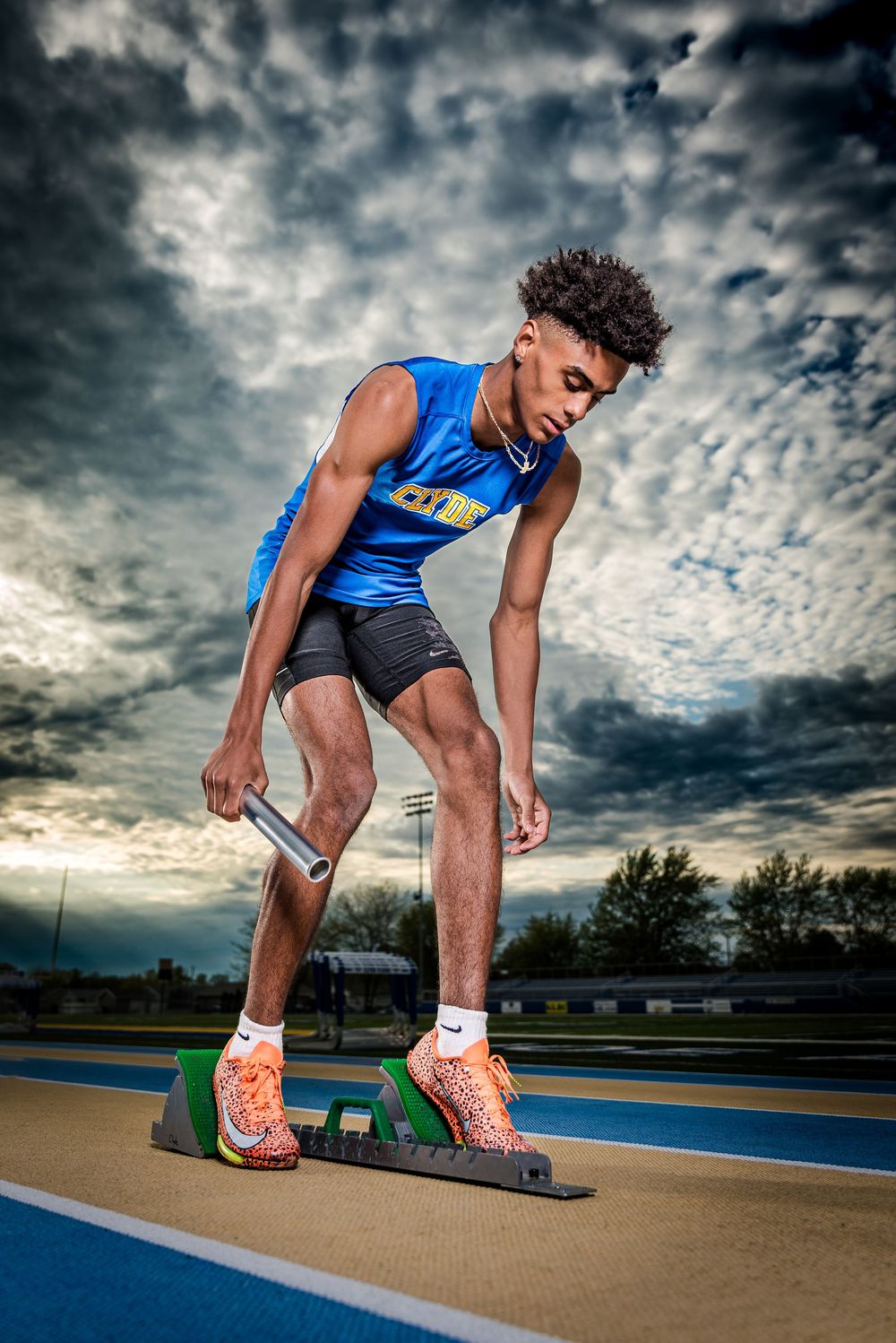 High school track runner preparing on starting block under dramatic sky – athlete portrait Ohio
