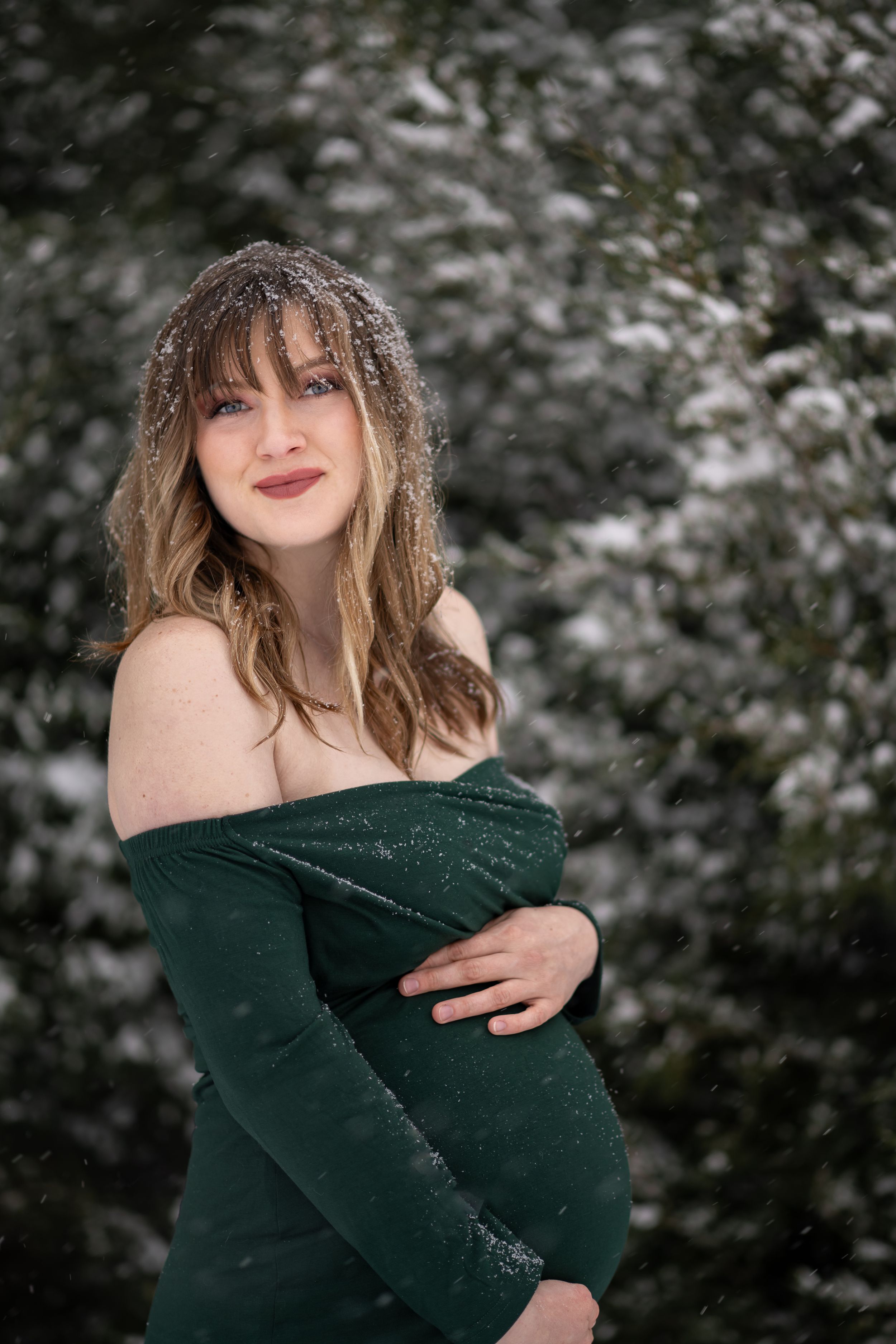 Person in a dark green sweater poses outdoors during snowfall with snowflakes in their hair.
