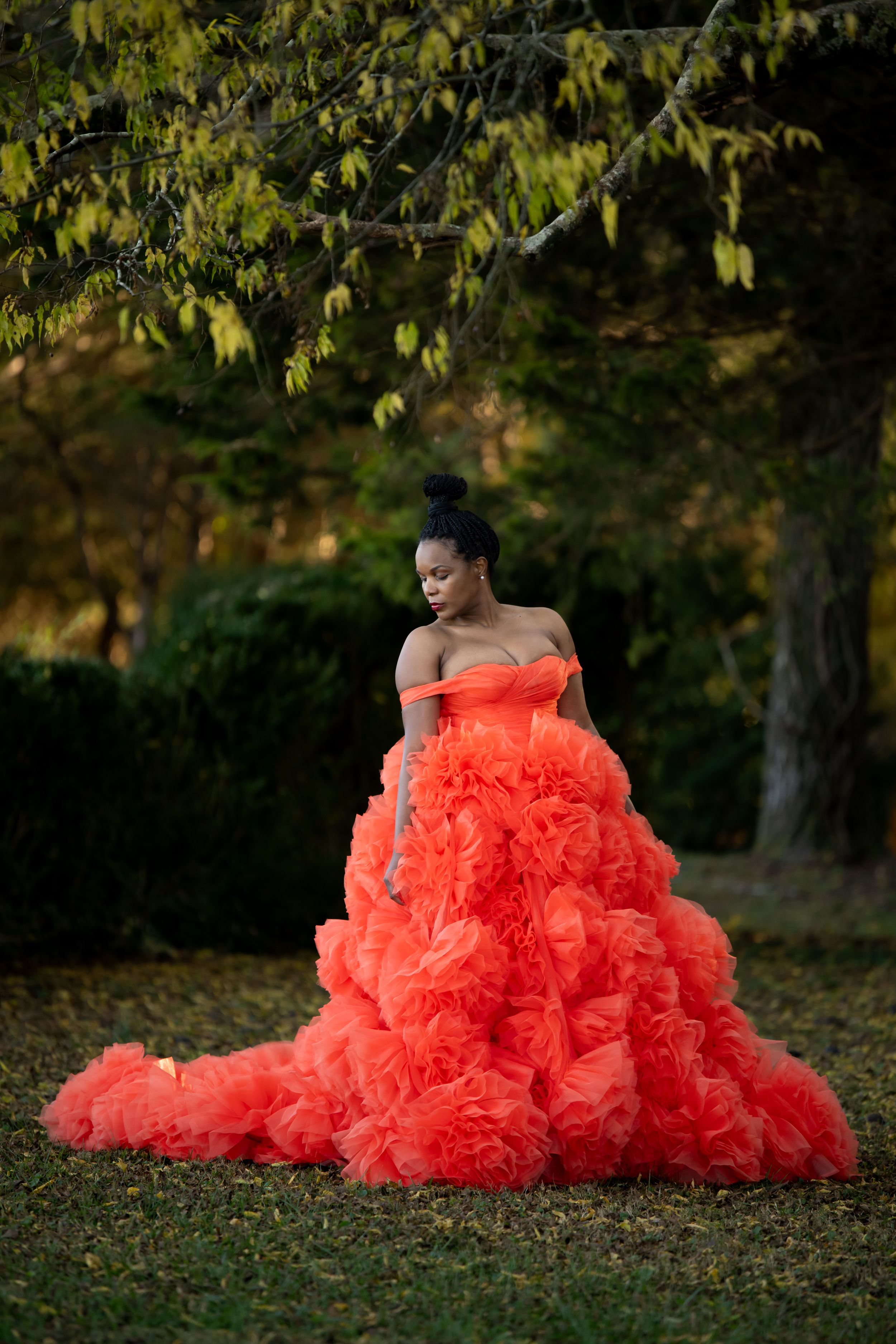 A stunning coral ruffled ballgown with dramatic layered tulle photographed outdoors against a natural woodland backdrop.