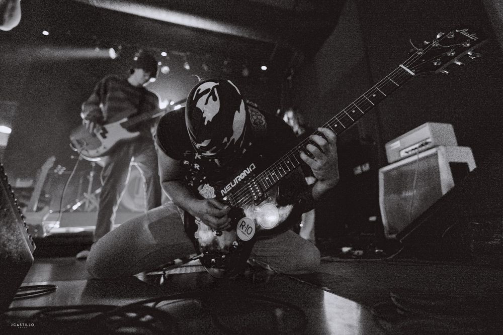 Black and white concert photo of guitarist performing on dark stage.