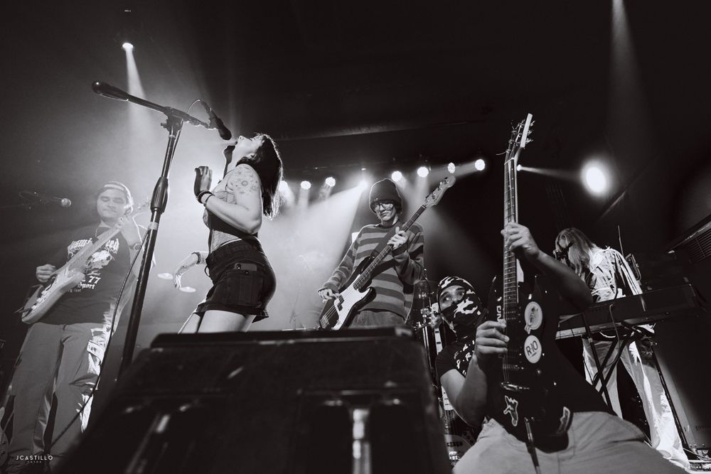 Black and white concert photo showing performers on stage with dramatic lighting and energetic movements.