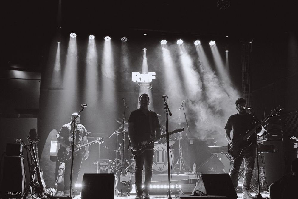 Band performing on stage with dramatic backlighting and smoke effects in black and white.