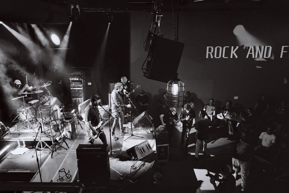Wide shot of rock band performing on stage with 'Rock and' text visible in the background.