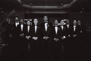 Groomsmen in formal black tuxedos stand in line for dramatic wedding photo.