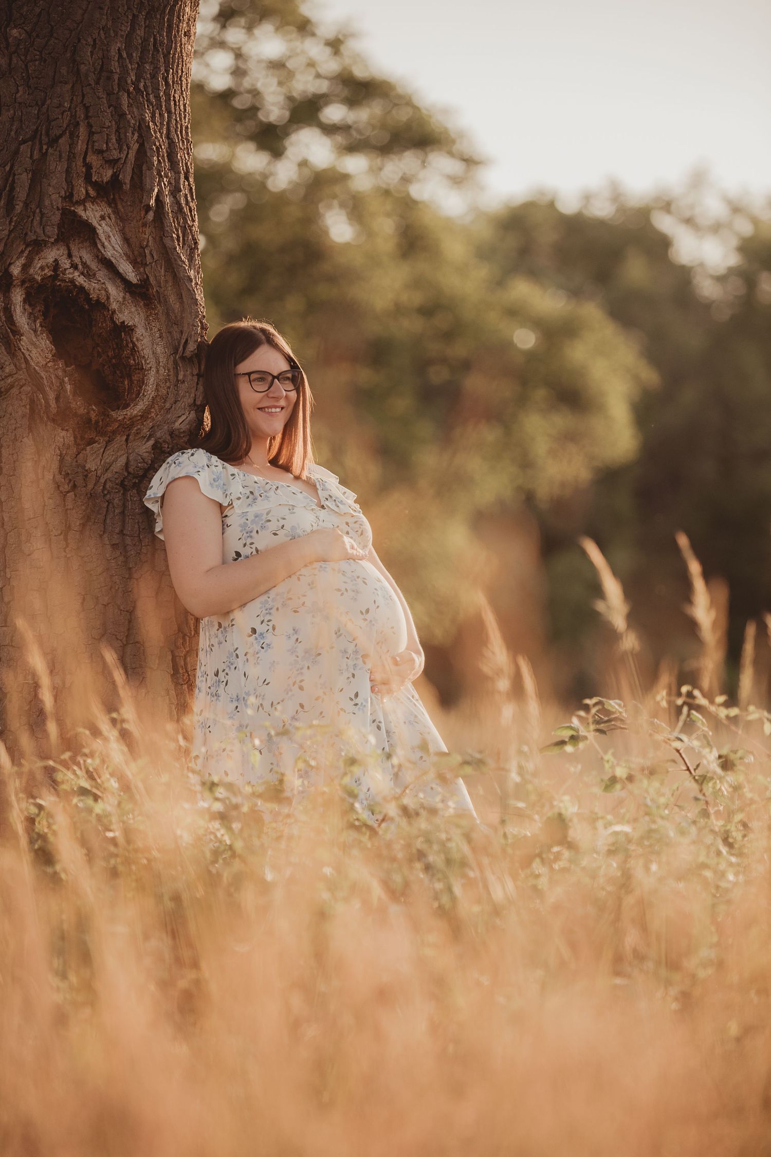 A figure in a floral dress sits in a golden field at sunset, creating a dreamy summer atmosphere.
