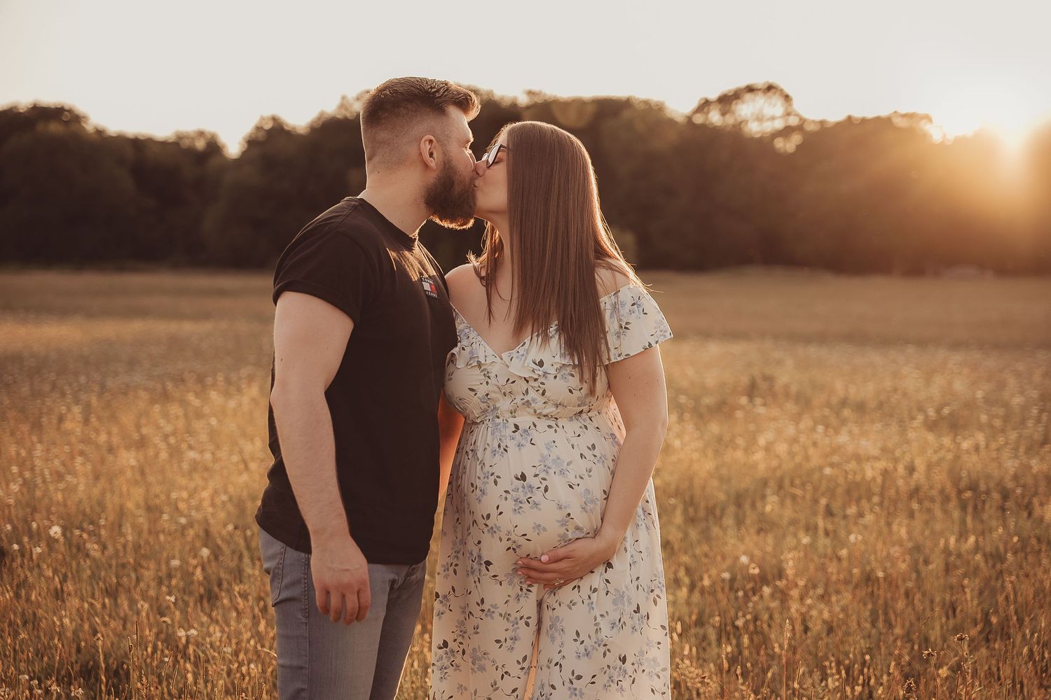 Couple embraces in a golden wheat field at sunset creating romantic silhouettes against the warm glowing sky.