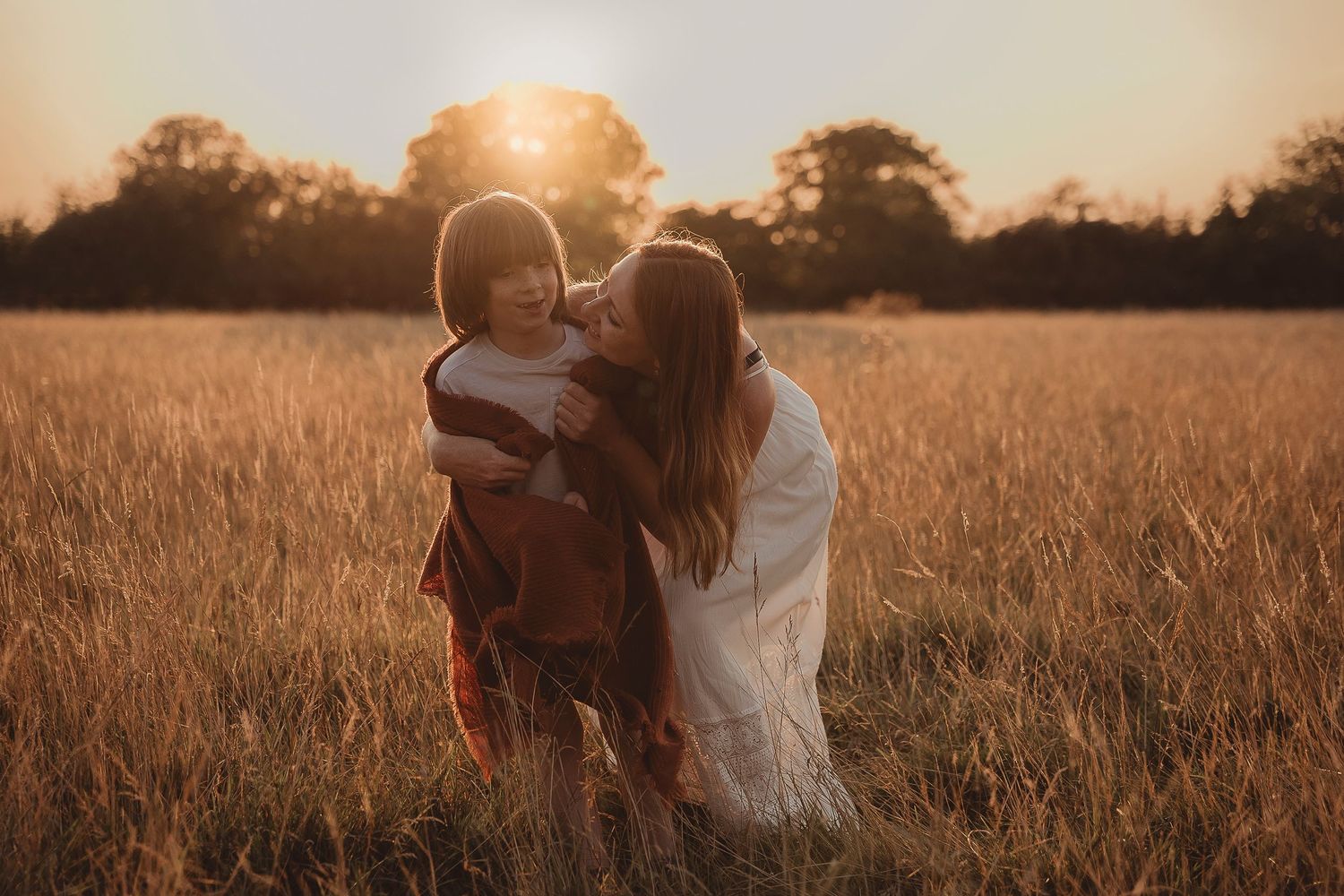 Two people embrace affectionately in a golden wheat field at sunset with warm backlighting creating a romantic atmosphere.