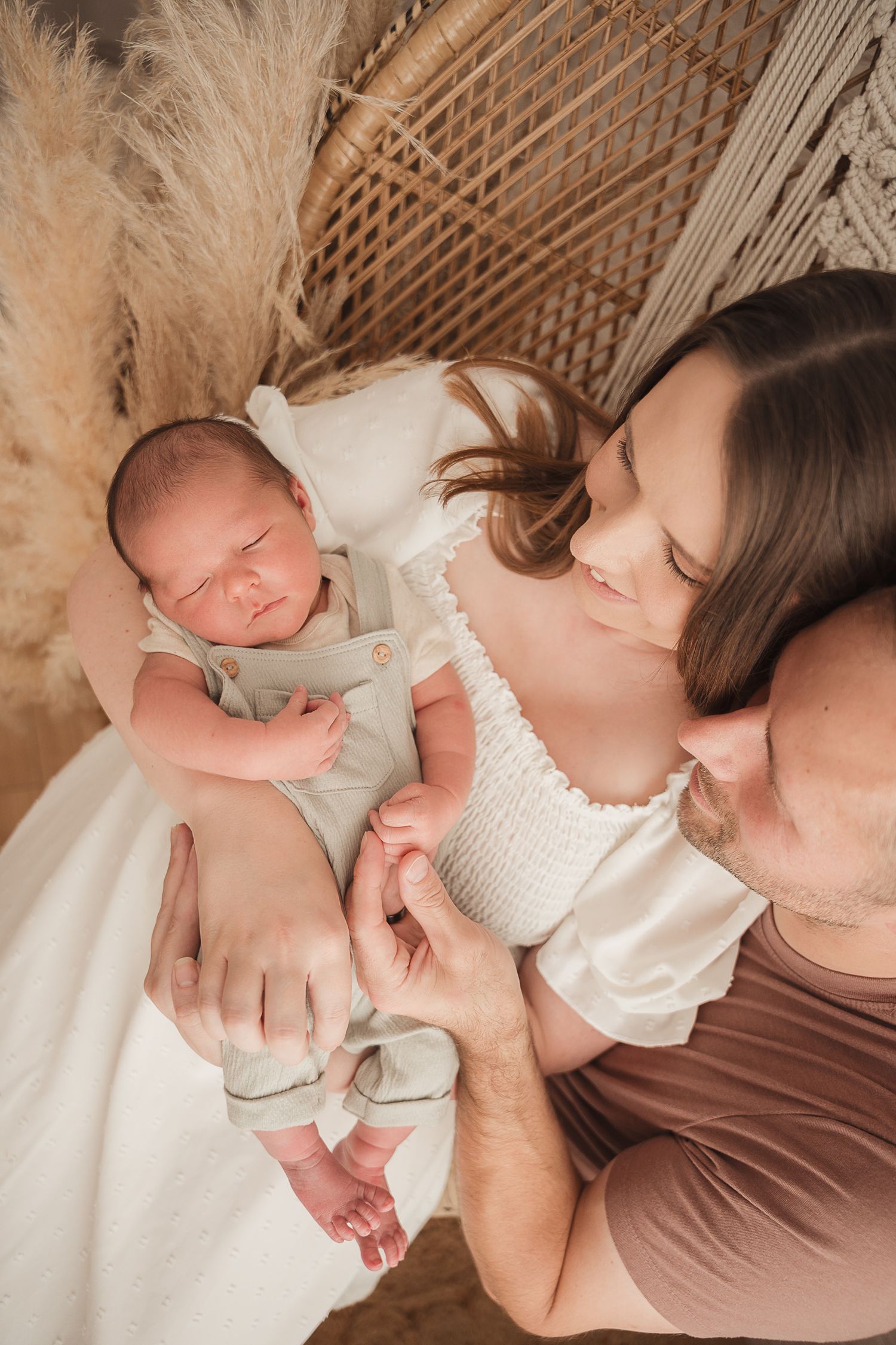 A tender moment captured between parent and newborn baby in white clothing against neutral tones.