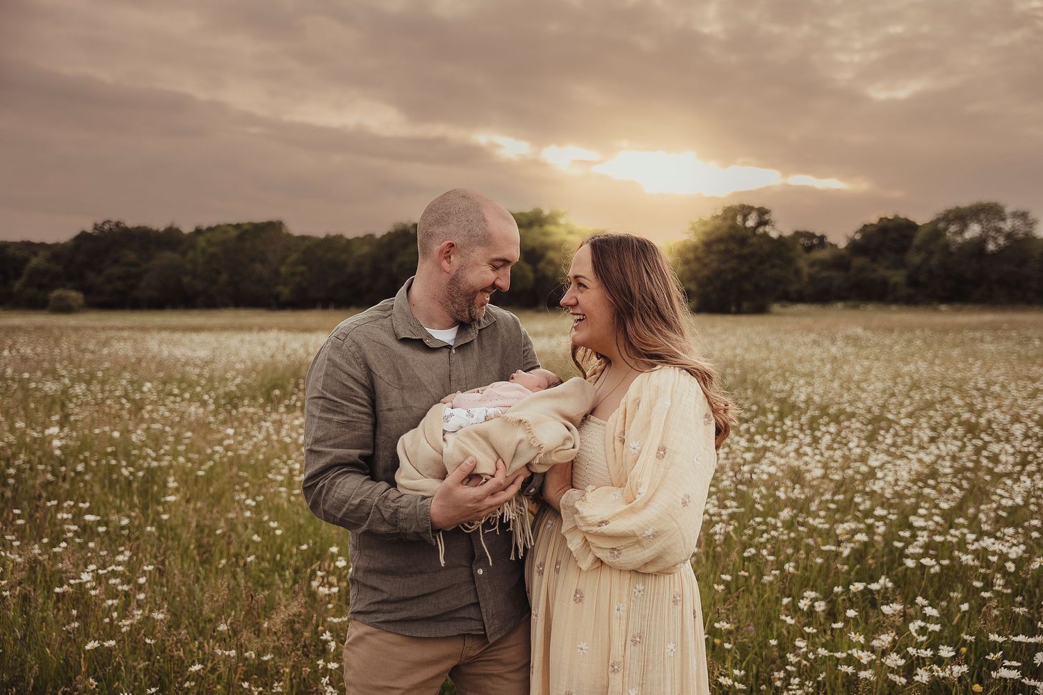 Loving couple embraces in golden sunlit meadow of blooming white wildflowers at sunset.