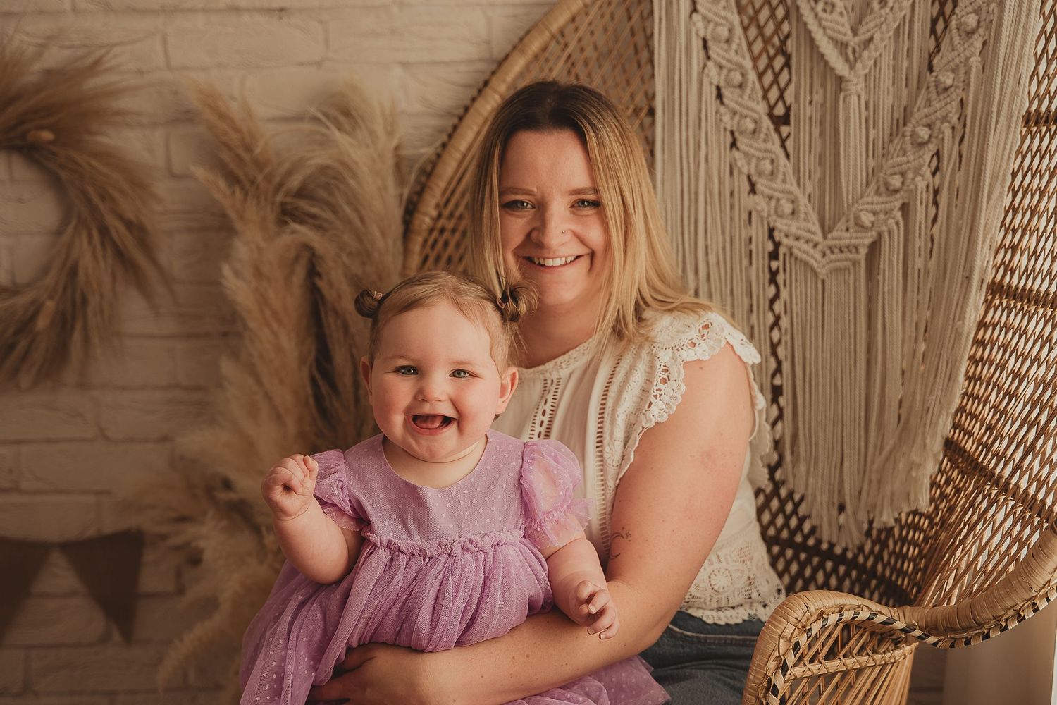A child and adult share joyful moments together on a rattan chair with macrame backdrop and natural lighting.