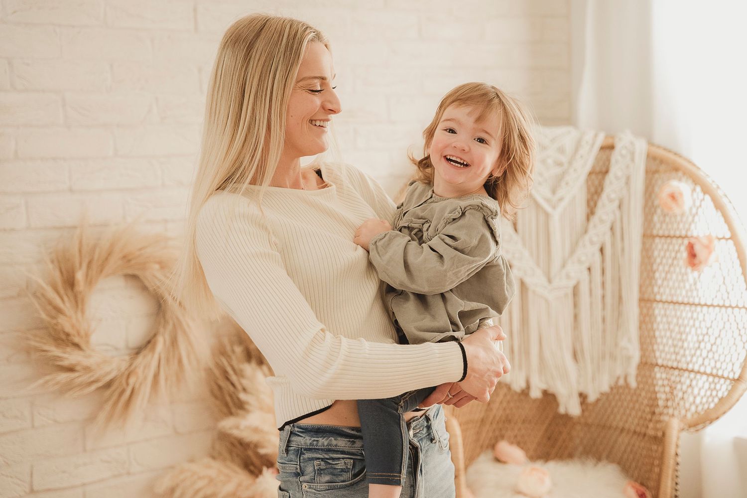 Sweet moment of parent and child laughing together in a bright room with boho decor and pampas grass.