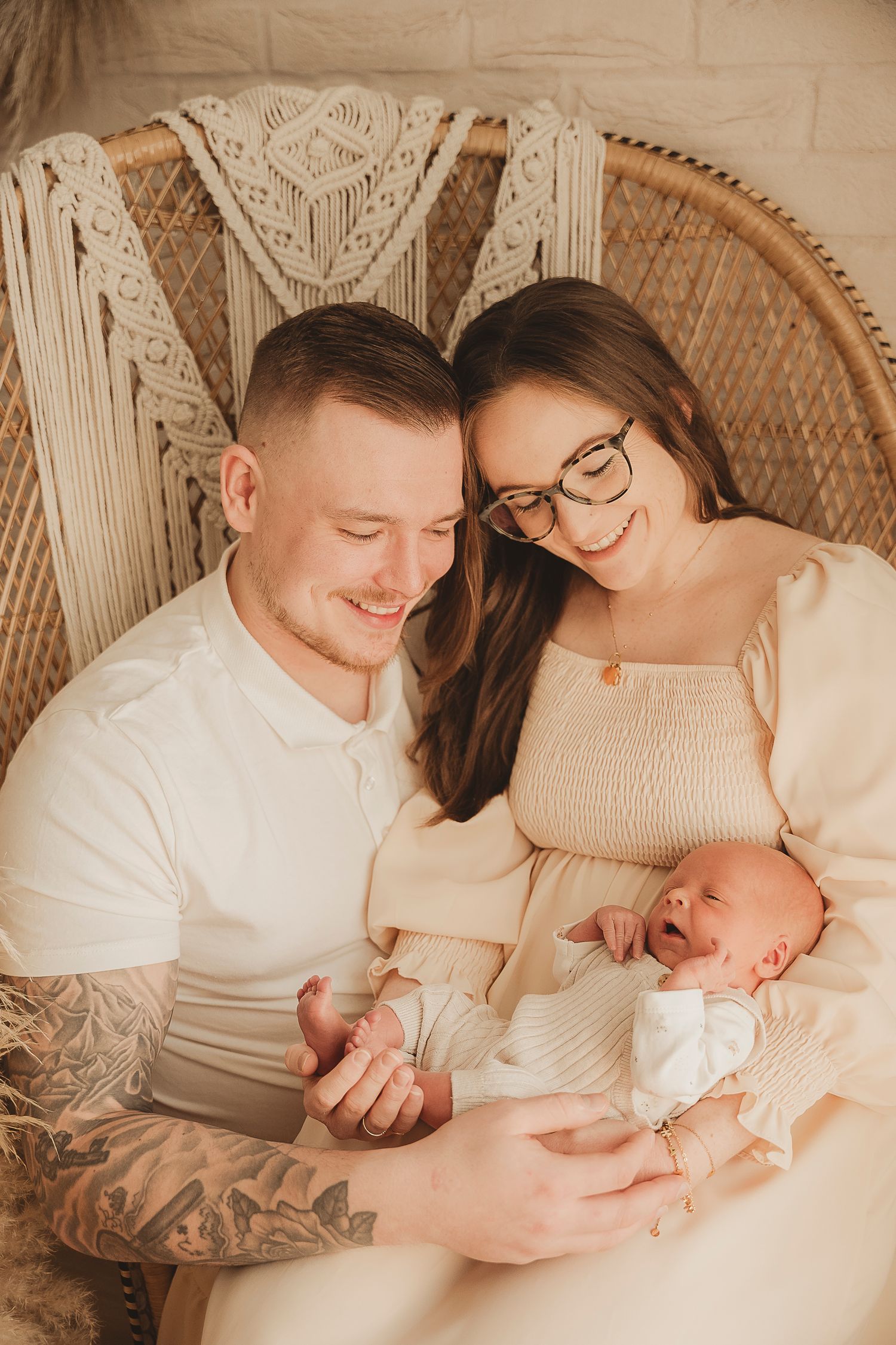 Intimate family portrait session showing tender moments with newborn baby in a warm neutral studio setting with macrame backdrop.
