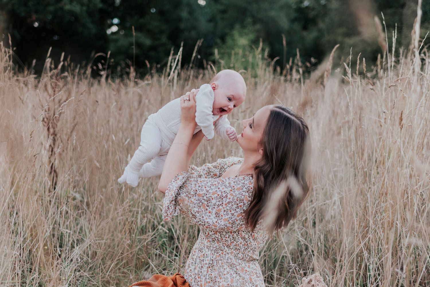 Mother and daughter in floral dresses share joyful moments while twirling together in a golden grass field.