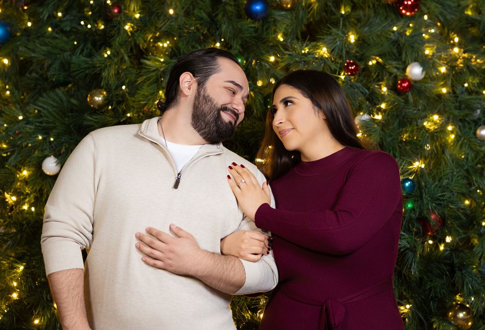 Four sequential photos showing a couple in burgundy and beige outfits embracing in front of a decorated Christmas tree.