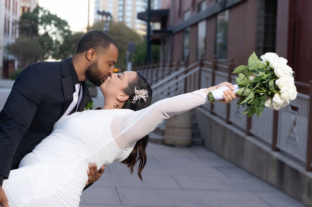 A couple in wedding attire sharing romantic kisses in front of a brick building.