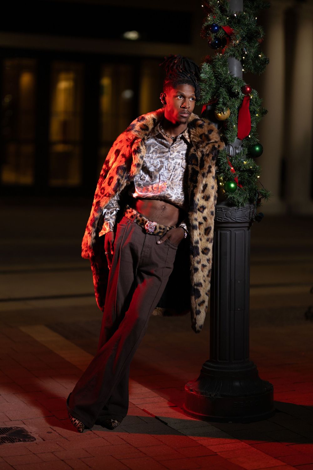 Stylish fashion photo at night featuring leopard print coat, red lighting and decorated Christmas tree by lamppost.