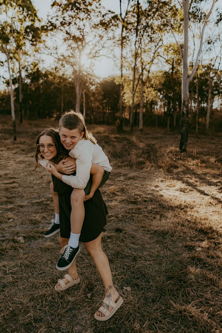 Parents swing young child by hands while walking along sunny rural dirt path together.