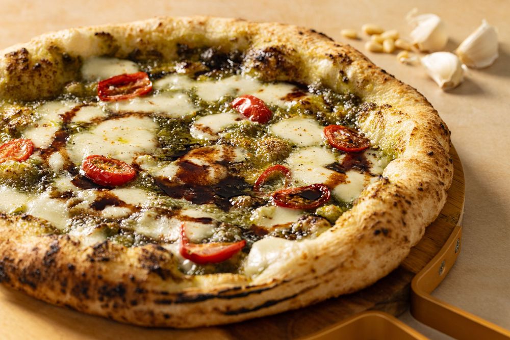 Pesto pizza topped with balsamic reduction and tomatoes served on wooden board and captured by Los Angeles food and lifestyle photographer.