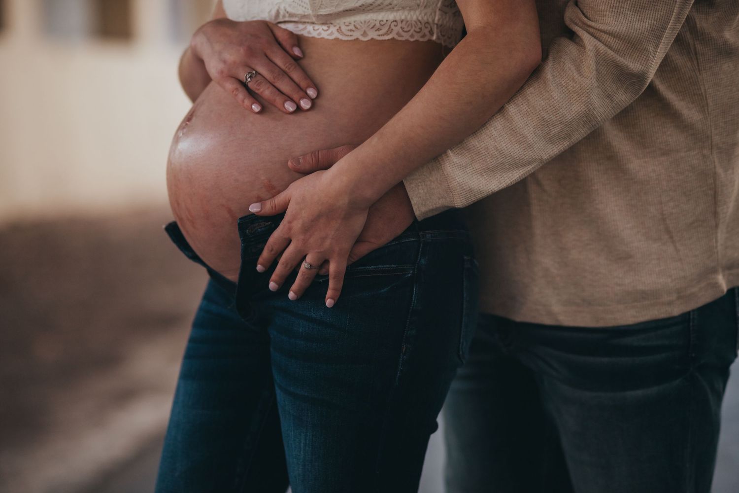 Close-up of hands gently resting on pregnant belly in natural lighting.