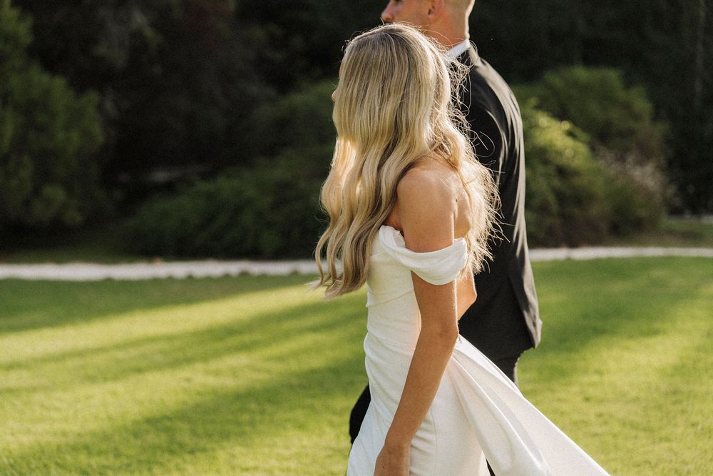 Bride and groom walking together outdoors, bride wearing elegant off-shoulder white wedding dress.