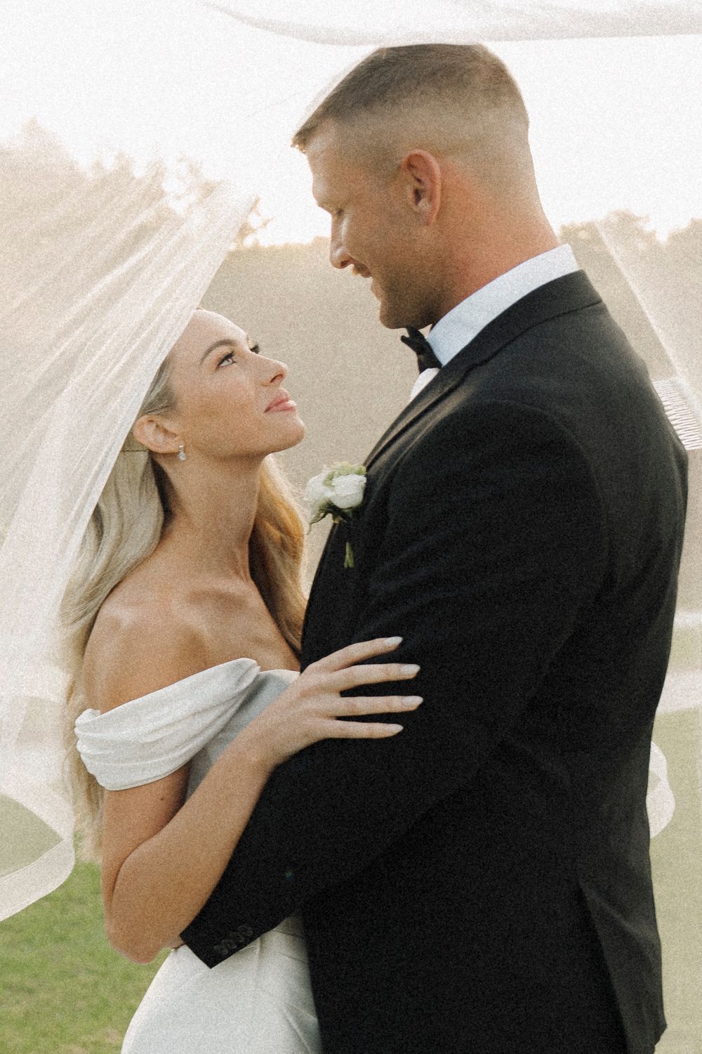 A bride and groom share a romantic moment under a flowing veil outdoors at their elegant wedding ceremony.