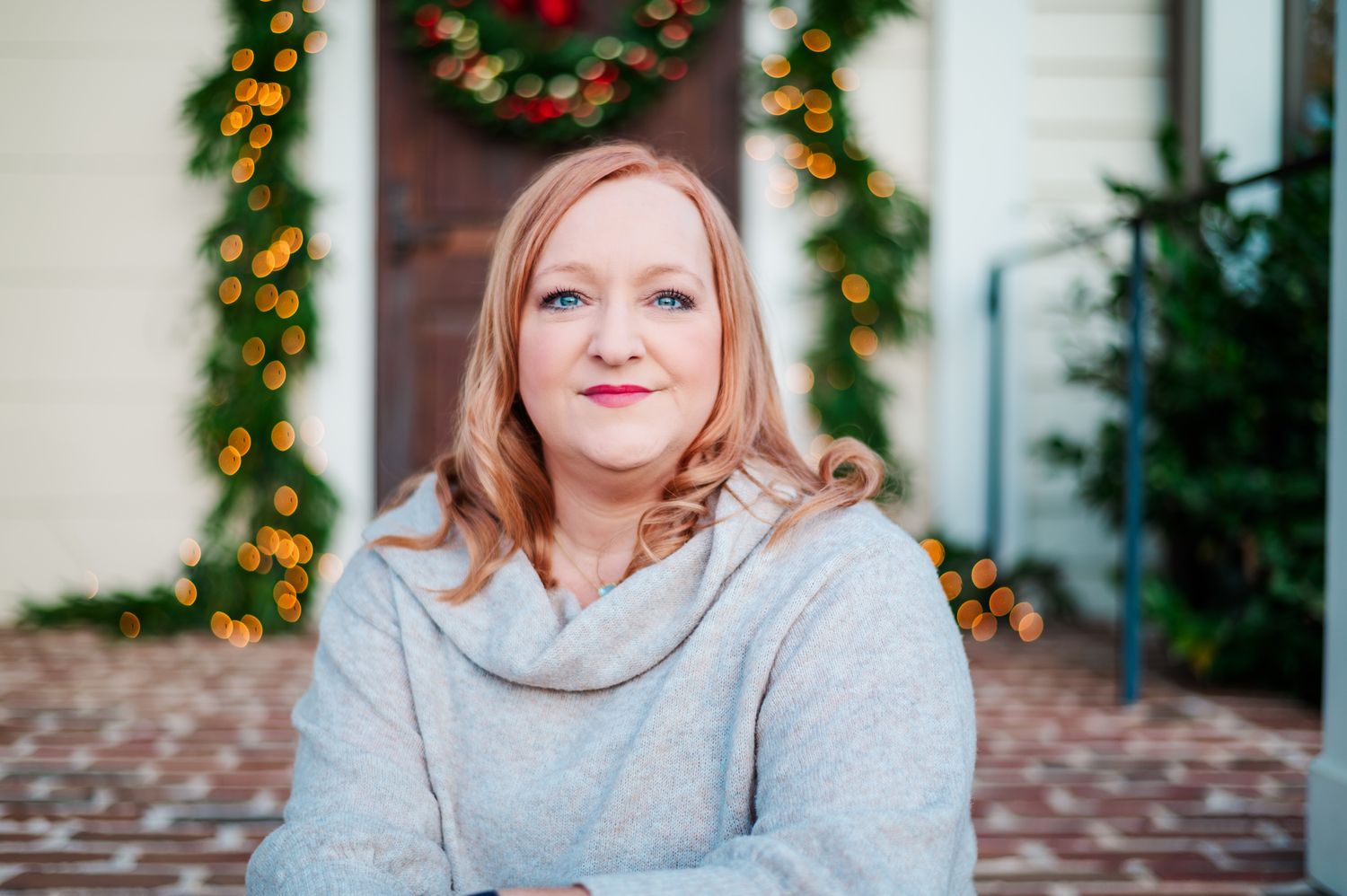 A portrait of someone in a gray sweater sitting in front of holiday decorations.