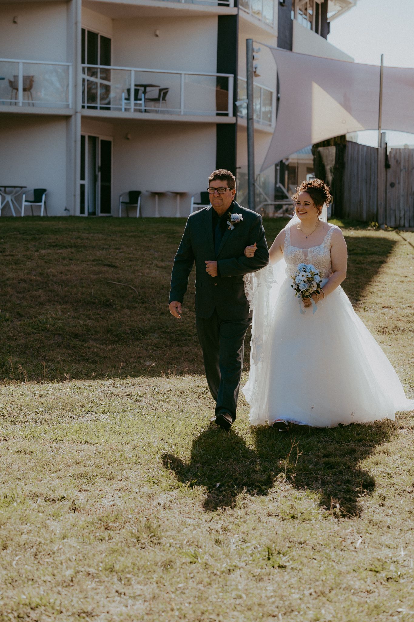 Bride in white ballgown walks down the aisle with her escort at an outdoor wedding.