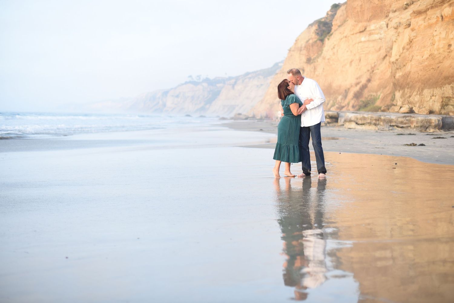 Couple embracing on La Jolla Shores beach with tall cliffs in background during sunset at California coastline. Torrey Pines. Scripps Pier.
