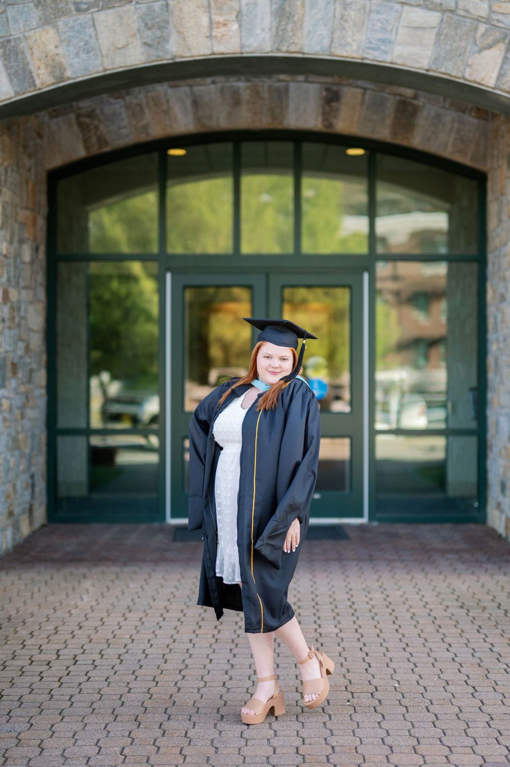 Graduate in cap and gown posing in front of stone archway entrance.